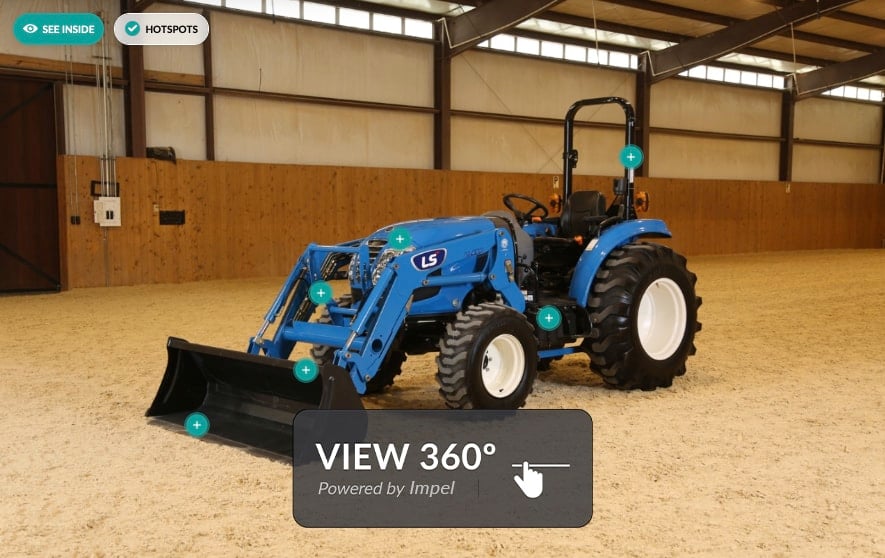 Ein blauer Traktor steht in einer geräumigen Halle auf einem hellen Boden. Der Traktor hat große schwarze Reifen und eine Schaufel vorne. Auf dem Bild sind mehrere grüne Symbole mit Pluszeichen zu sehen, die auf verschiedene Teile des Traktors hinweisen. Oben links befinden sich die Schaltflächen See Inside