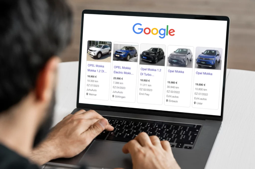 Ein Mann tippt auf einem Laptop. Auf dem Bildschirm ist eine Google-Suche nach verschiedenen Modellen des Opel Mokka zu sehen, mit Preisen, Kilometerständen und Standorten wie Weimar, Göttingen, Einbeck und Uslar.